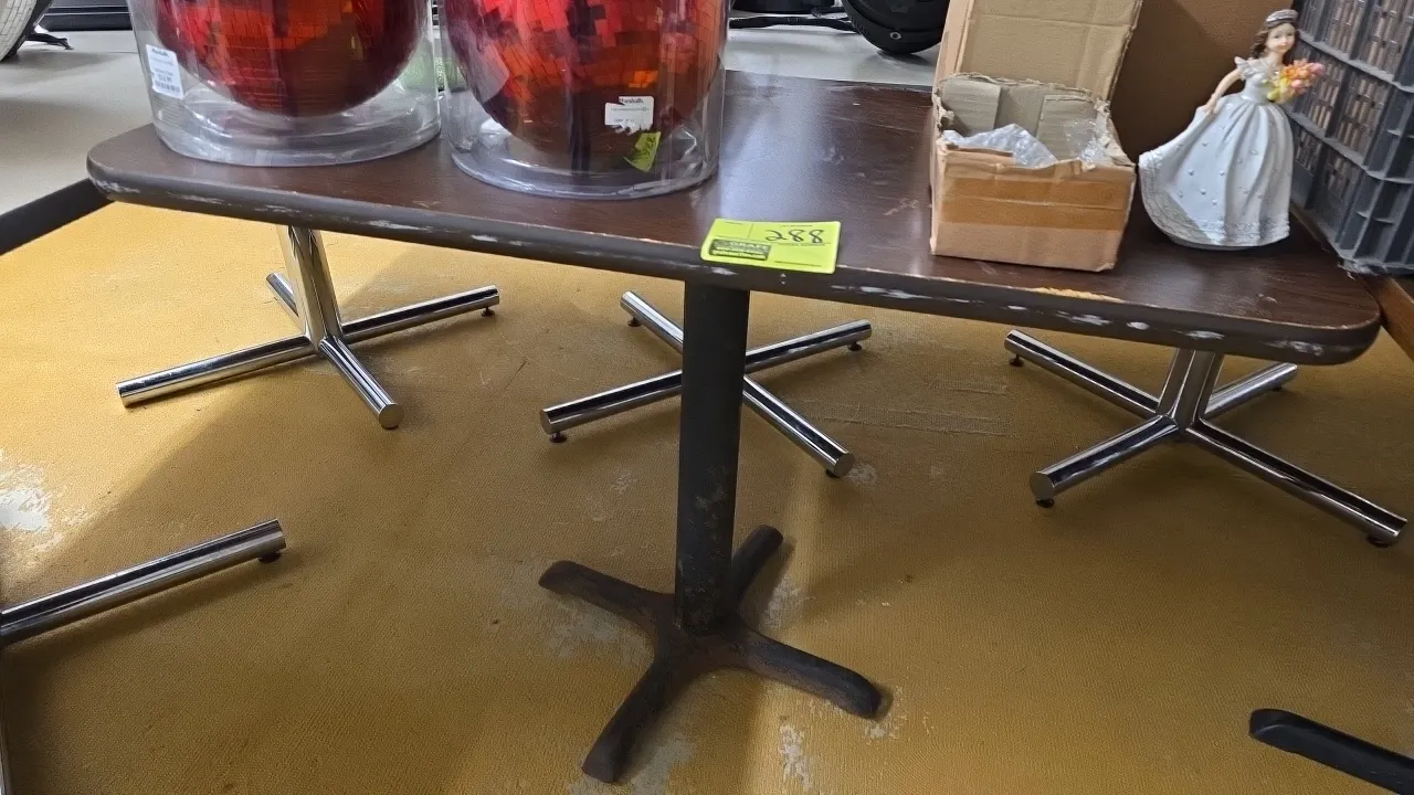 Laminate dining table. Features a woodgrain laminate top and rounded corners. 41.5" x 24". Mounted on a pedestal X-base. Contents not included.