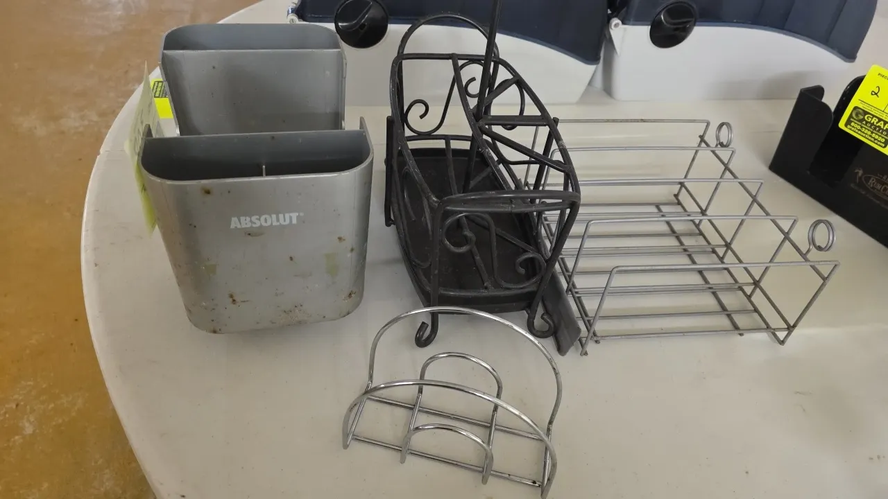 Assorted poly and metal condiment holders and bar caddies. Includes (1) Absolut branded plastic bar caddy organizer, (1) black metal scrollwork condim