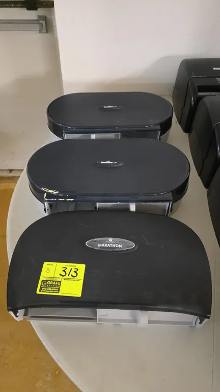 Marathon dual-roll bathroom paper dispensers. Features black plastic covers, dual-roll capacity, and serrated cutting edges. Designed for wall mountin