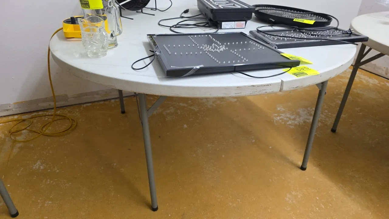 Round polyethylene fold-in-half folding table. Features a white molded plastic top and folding gray metal tubular legs. 60"Dia. Contents not included.