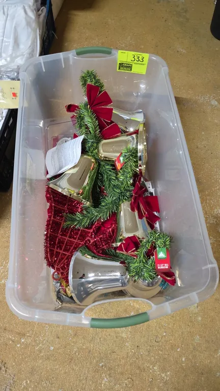 Plastic storage tote with Christmas decor and Santa apparel. Includes a clear poly storage tote, decorative metallic bells with artificial greenery an