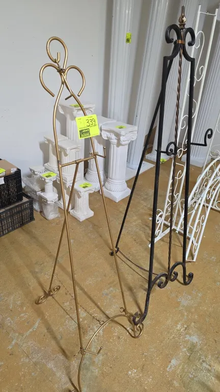 Decorative metal display easels. Features scrollwork accents, display hooks, and chain rear leg stays. Includes one gold-tone metal easel and one dark