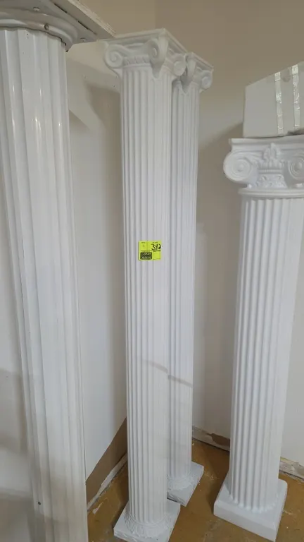 White decorative poly Roman columns (set of 2). Features molded polyethylene construction with fluted shafts, Ionic-style capitals, and square bases.