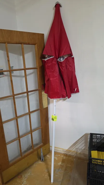 Patio table umbrella. Features a red fabric canopy with white trim, silver-tone interior lining, and collapsible frame. Mounted on a white metal pole