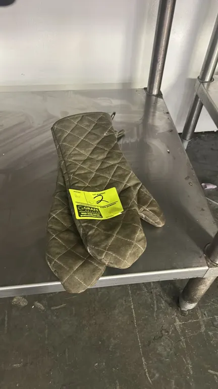 Pair of quilted oven mitts. Features heat-resistant fabric construction and hanging loops. Table not included.