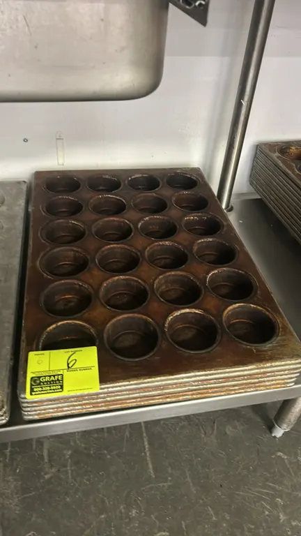 Commercial 24-cup metal muffin pans. Features a 24-cavity layout arranged in a 4 x 6 pattern with wire-reinforced rims.