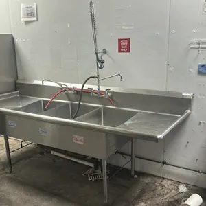 Stainless steel 3-compartment sink. Features left and right drainboards, integrated backsplash with left side splash, two splash-mount faucets, and an