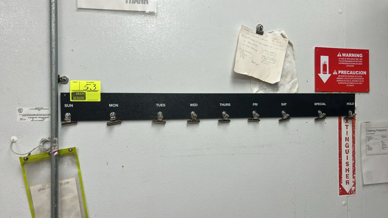Poly wall-mounted schedule organizing rack. Features a textured black poly strip with 9 metal clips labeled SUN, MON, TUES, WED, THURS, FRI, SAT, SPEC