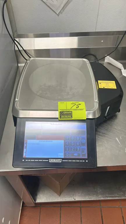 Hobart HTs-7LS commercial label-printing scale. Features touchscreen operator interface, integrated thermal label printer, and stainless steel weigh p