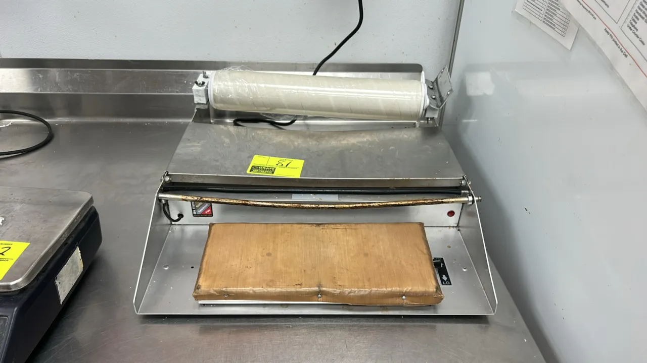 Heat Seal single bar film wrapper. Features stainless steel construction, heated sealing plate, cut-off rod, and film dispenser with roll. Electrical: