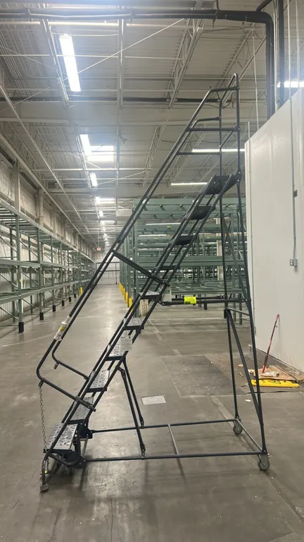 Tri-Arc 100" metal rolling warehouse ladder. Features 10 perforated steel slip-resistant steps, dual handrails, top safety guardrail, and foot-actuate