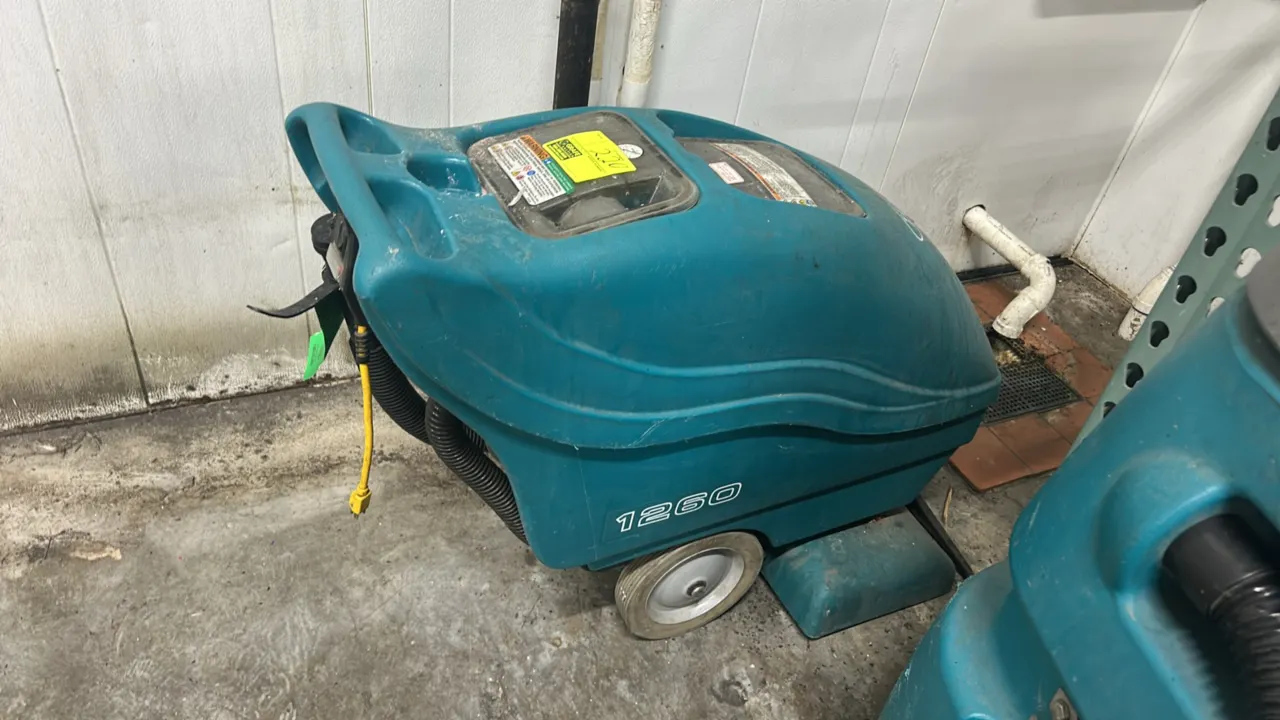 Tennant 1260 self-contained commercial carpet extractor. Features front vacuum pickup shoe, dual clear tank access lids, rear drain hose, and integrat