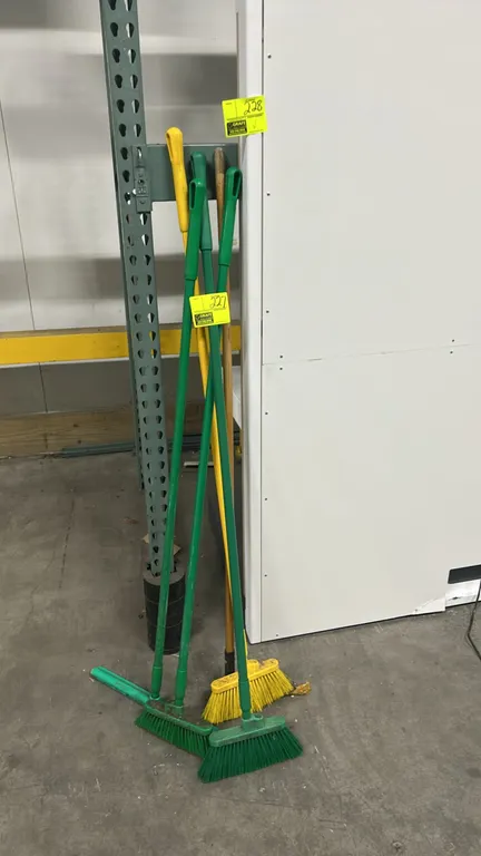 Assortment of commercial cleaning brooms. Includes color-coded synthetic bristle upright brooms and handles. Pallet racking and background items not i
