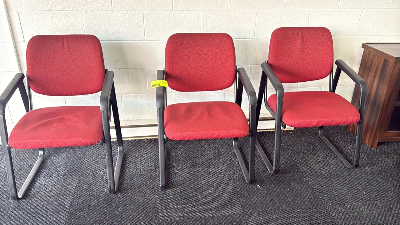 Upholstered office guest armchairs. Features red patterned fabric padded seat and backrest with black armrests. Mounted on a black metal sled cantilev