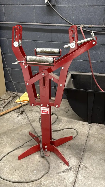 Branick 5045 manual tire spreader. Features dual tire rollers, adjustable spread arms, and gas spring assist. Mounted on a steel floor pedestal stand.