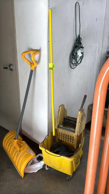 Commercial mop bucket with wringer, mop, and shovel. Features a yellow molded plastic bucket with wringer assembly mounted on swivel casters, mop with