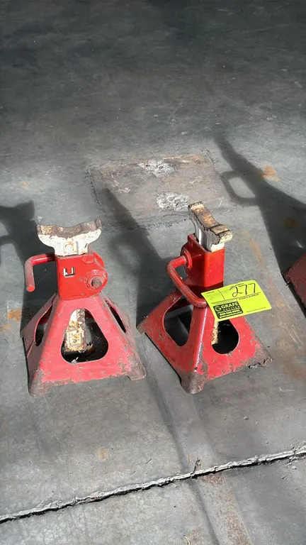 Floor jack stands. Features steel construction with red painted finish, ratcheting height adjustment columns, locking release handles, and four-leg py