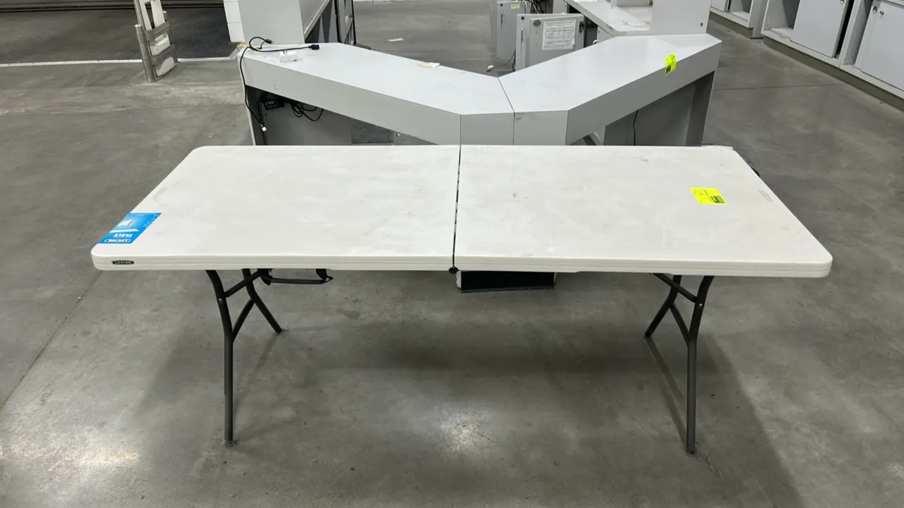 Lifetime fold-in-half folding table. Features a white polyethylene top and folding metal legs with an integrated carry handle. 6'L.