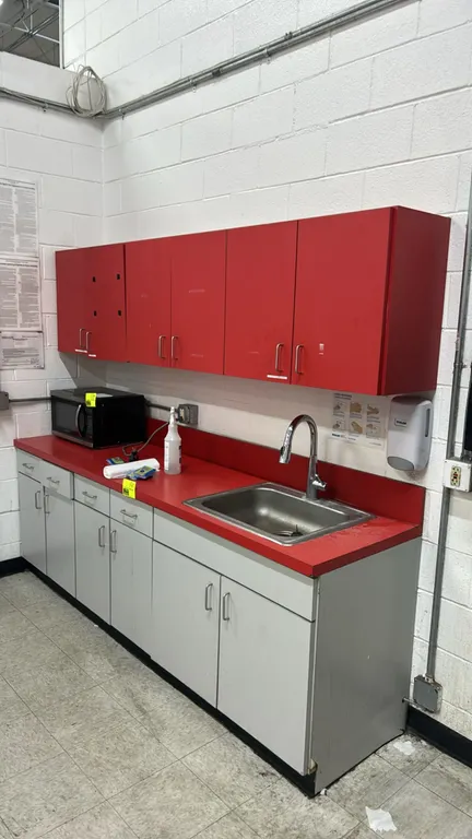 Laminate breakroom cabinets with stainless steel sink. Includes upper red laminate wall-mounted cabinets and lower gray laminate base cabinets with dr
