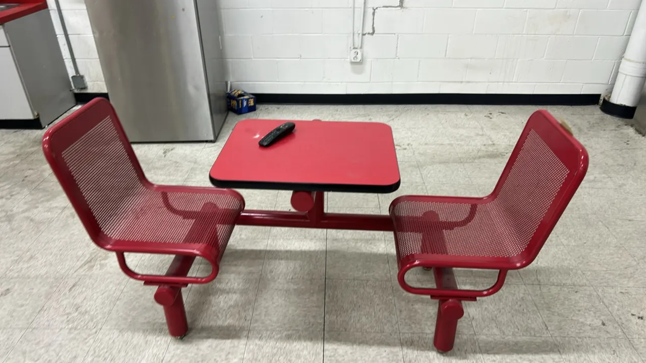 Laminate lunch table with attached metal chairs. Features a red laminate top with black protective edge and (2) red perforated metal seats mounted to
