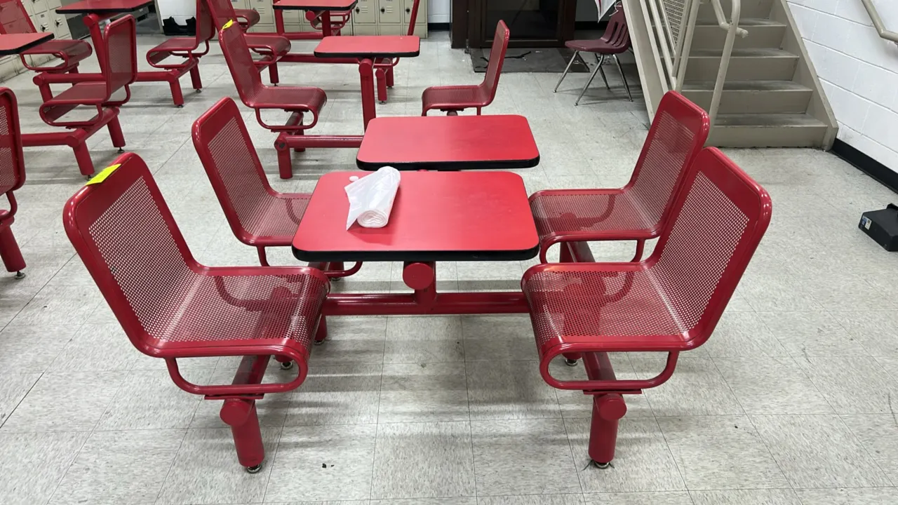 Laminate cafeteria lunch tables with attached metal chairs. Features red laminate tabletops, tubular metal frames, and (2) attached perforated metal s
