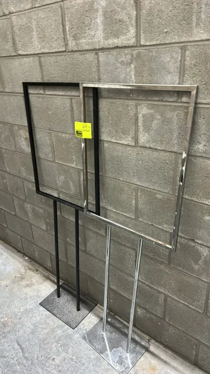 Metal sign stands. Features one chrome finish and one black finish stand with rectangular sign frames and dual upright posts. Dimensions: 22"W. Mounte