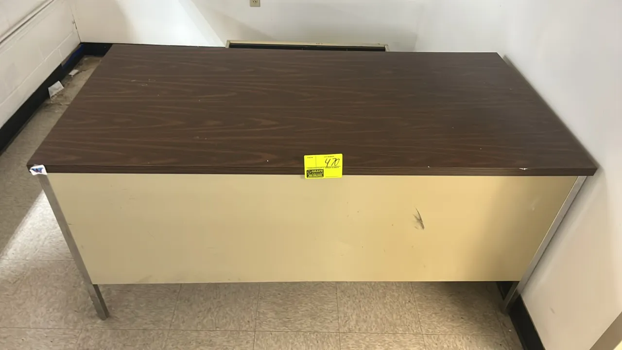 Double-pedestal desk. Features a woodgrain laminate top, center drawer with organizer tray, five pedestal drawers, and chrome legs. Tan metal base. 60