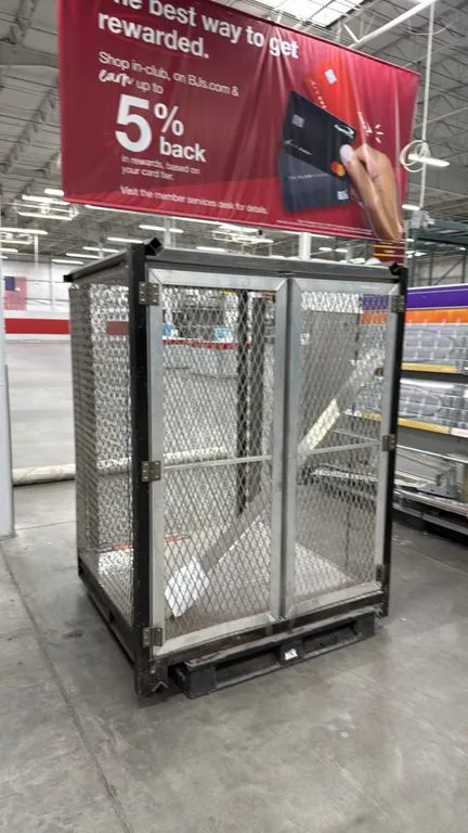 Metal pallet cage. Features expanded wire mesh construction, dual hinged front doors, mesh top, and integrated pallet base. Dimensions: 52.5" x 48" x