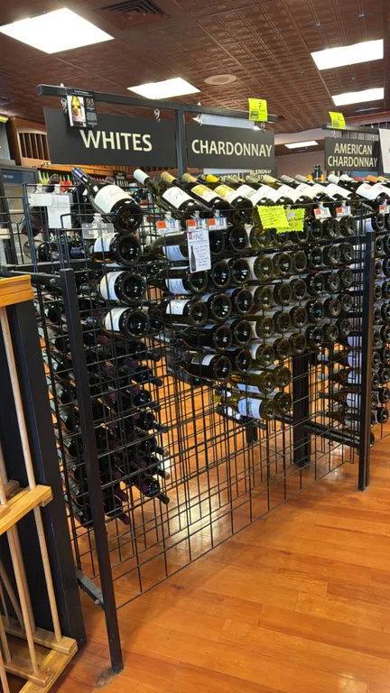 Dual-sided metal wine merchandiser. Features black wire grid construction, dual-sided bottle display racks, angled top presentation tier, and overhead
