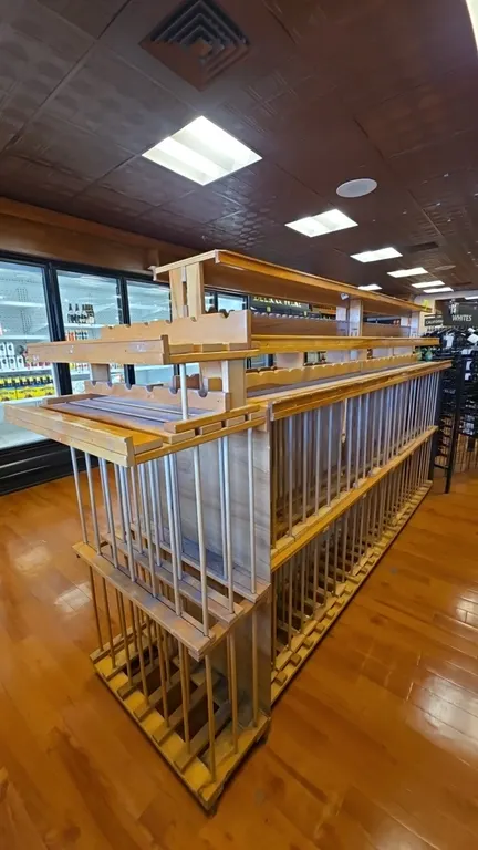 Dual-sided wood wine display merchandiser. Features multi-tier bottle storage with vertical dowel dividers and upper cradle display shelving. Dimensio