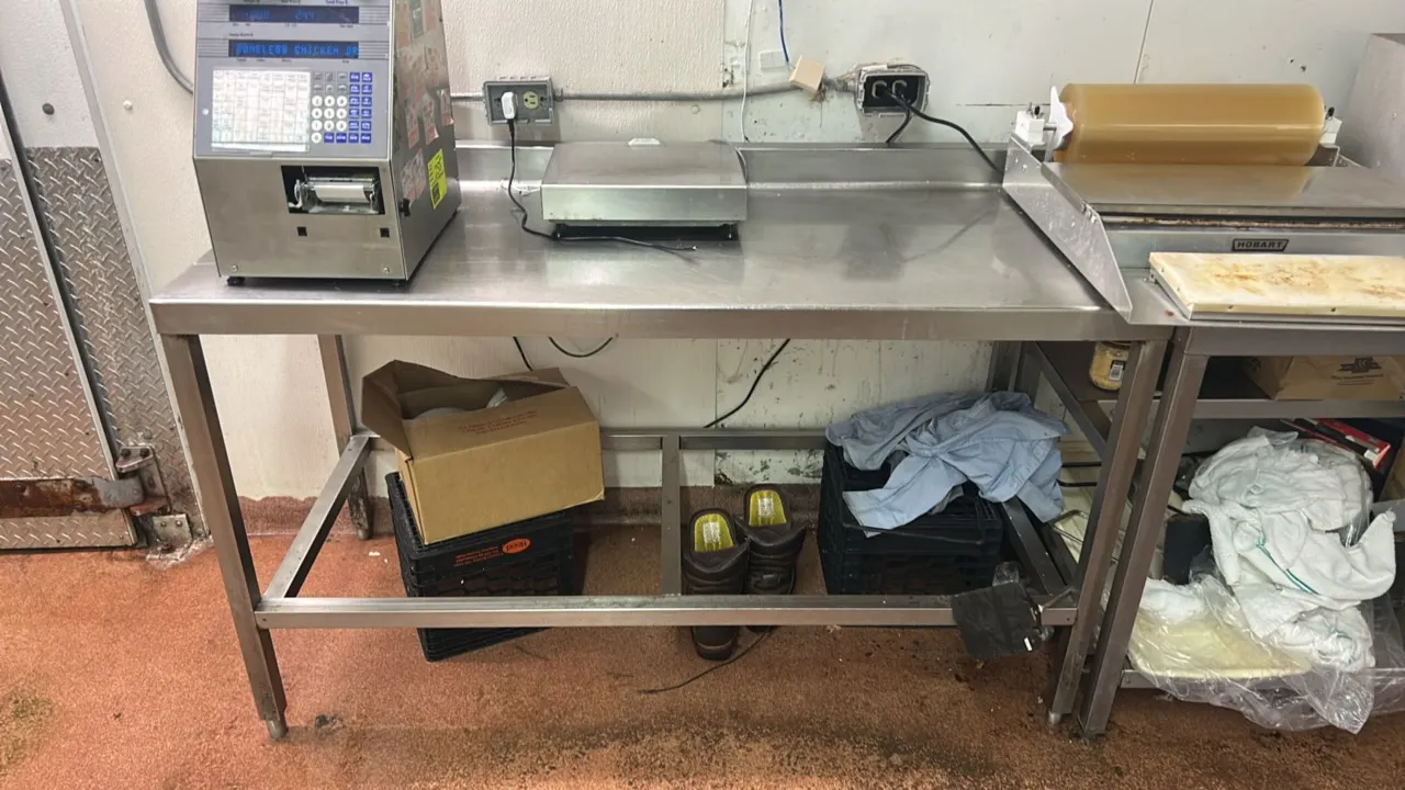 Stainless steel work table with rear backsplash. Features stainless steel construction, open lower frame, and square legs with adjustable feet. Dimens