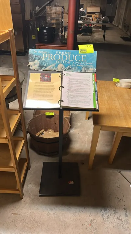 Freestanding metal menu and display stand. Features an angled top surface with ring binder attachment, top signage bracket, and black metal constructi