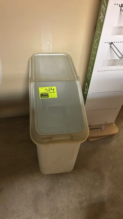 Poly portable ingredient bin. Features white polyethylene construction with a clear sliding lid. Mounted on casters. Display rack in background not in