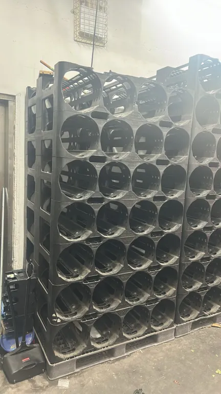 Quantity of PSI modular polyethylene 4-bottle water jug storage racks. Features molded 4-compartment bottle cradles per tier, designed for multi-gallo