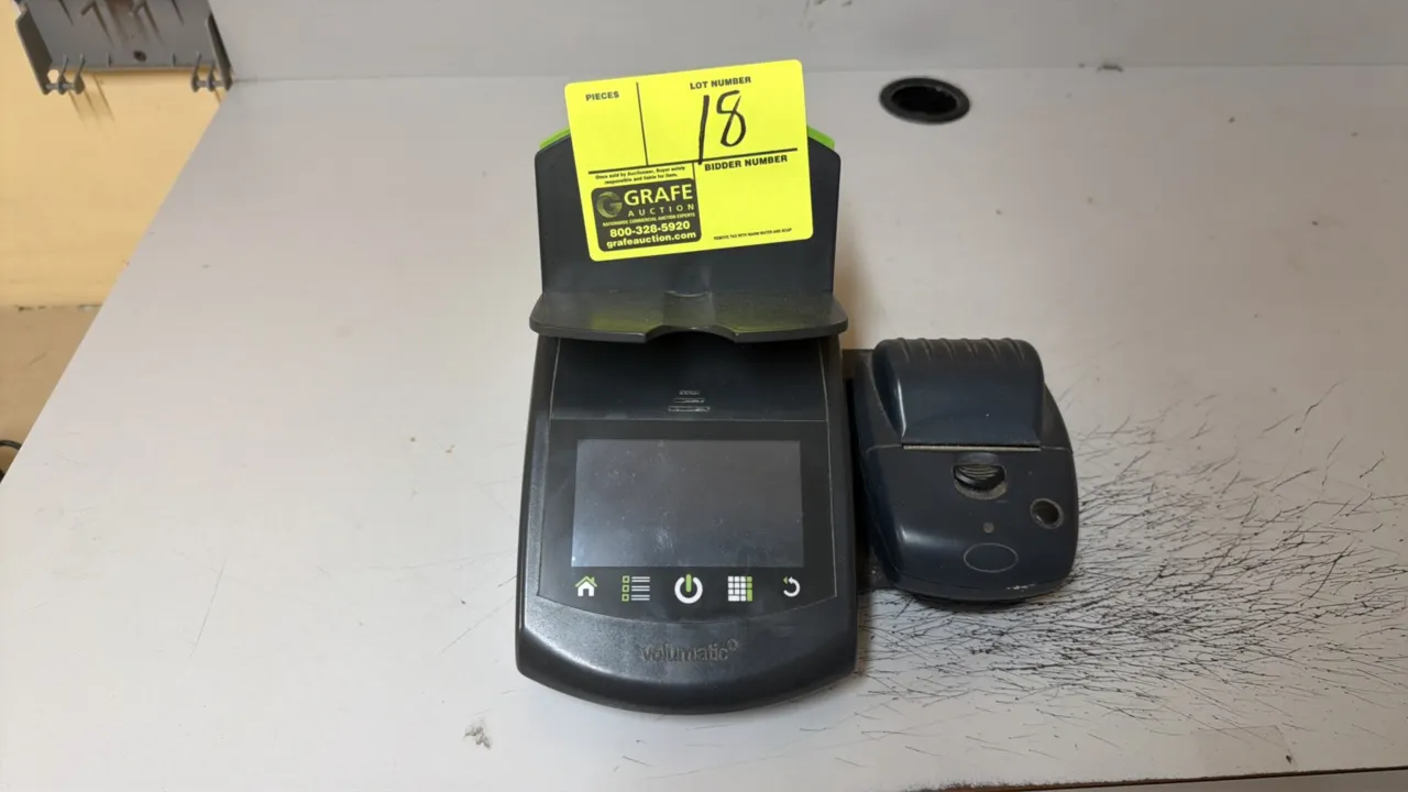 Volumatic money counting scale. Features digital display, button controls, bill and coin tray, and attached receipt printer.