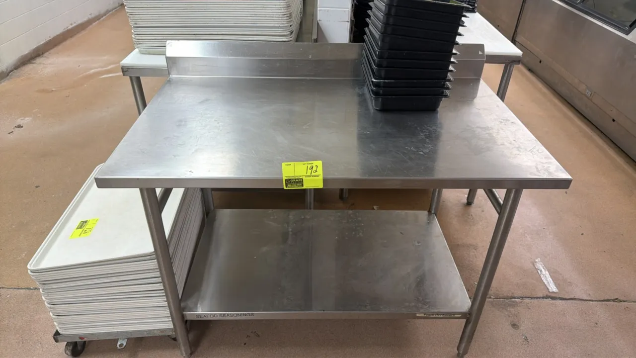 Stainless steel work table. Features rear backsplash and lower undershelf. 4'L x 2.5'W. Mounted on tubular legs with adjustable bullet feet. Contents