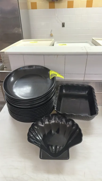 Assorted black polymer deli display bowls. Includes a stack of round shallow bowls, a fluted rectangular display pan, and a scalloped shell bowl.