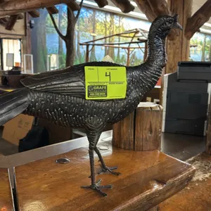 Metal wild turkey decorative sculpture. Features textured metal plumage, layered wings, and tall standing legs with splayed feet. Freestanding design.